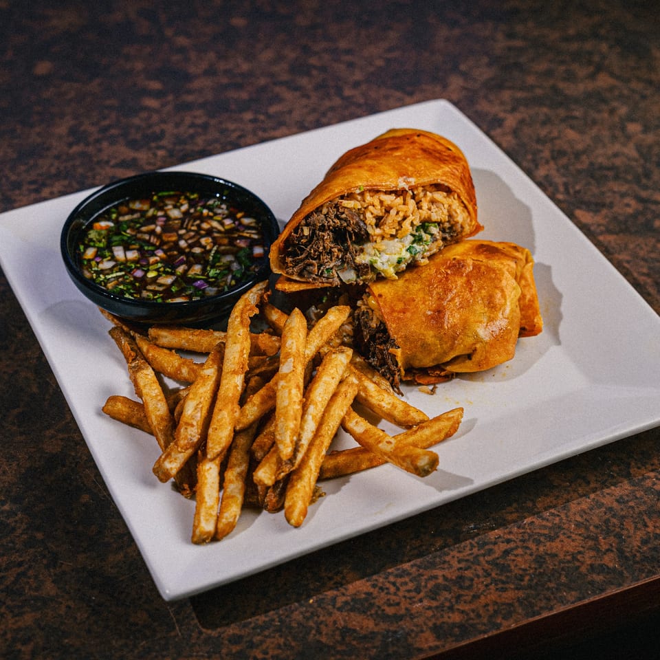 A golden-fried burrito, cut in half to show beef and rice filling, with fries and dipping sauce.