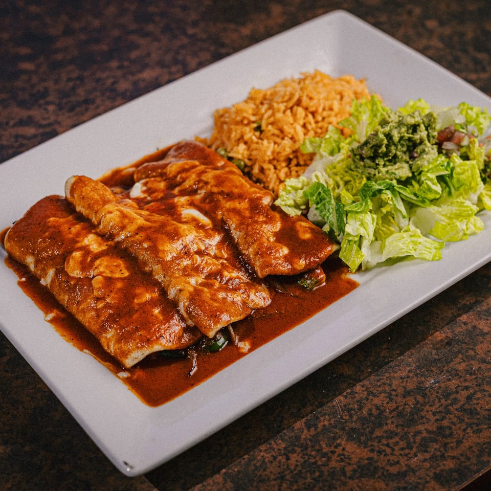 Three enchiladas covered in red sauce and cheese, with rice, lettuce, and guacamole on a white plate.