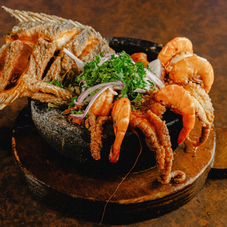 Fried fish, shrimp, and octopus with cilantro and red onion in a stone bowl.